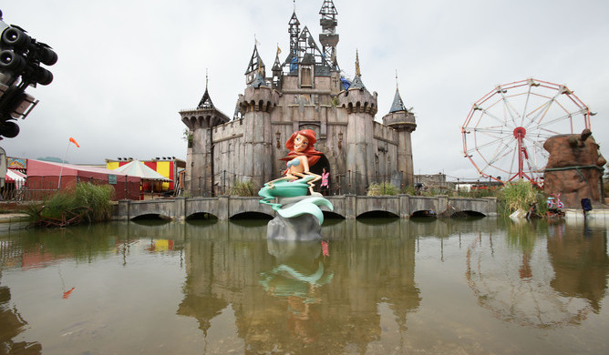 A mermaid piece by Banksy, with a castle by Banksy and Block 9 in the background, during the press view for the artistâs biggest show to date, entitled 'Dismaland', at Tropicana in Western-super-Mare, Somerset.